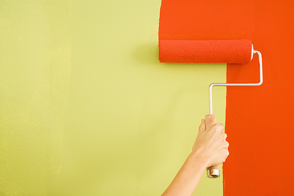 Caucasian female hand painting red over a green wall.